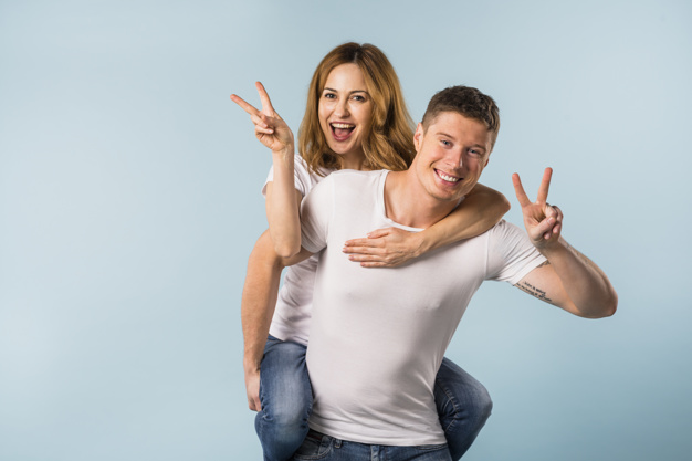 retrato-de-um-sorrindo-namorada-montando-ligado-seu-namorado-costas-mostrando-sinal-vitoria_23-2148056274